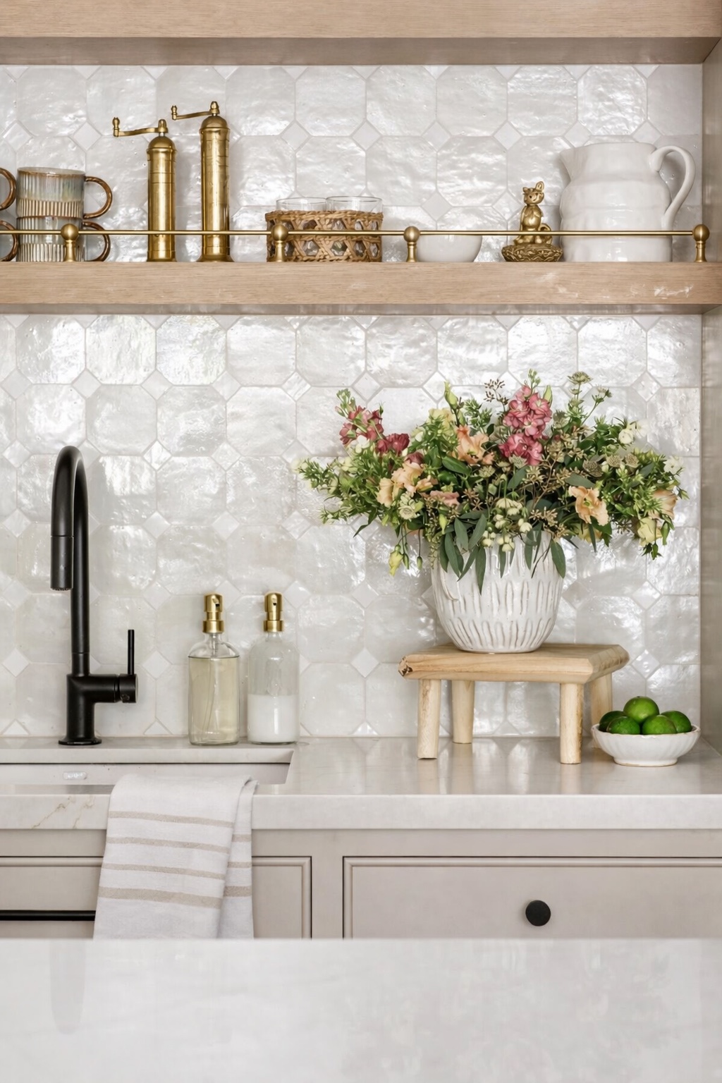Kitchen detail with glossy tile backsplash, floating wood shelf, black faucet, and fresh flowers.